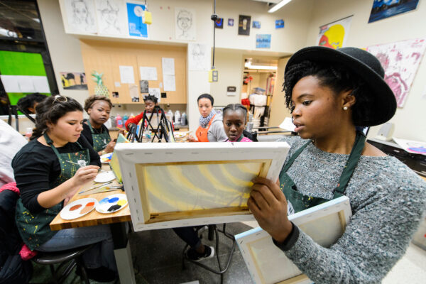 A person showing a painted canvas to a group of people sitting at a table