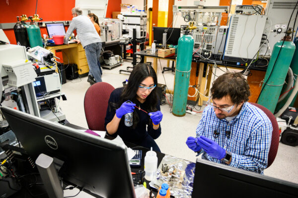 Two people wearing gloves and handling research equipment