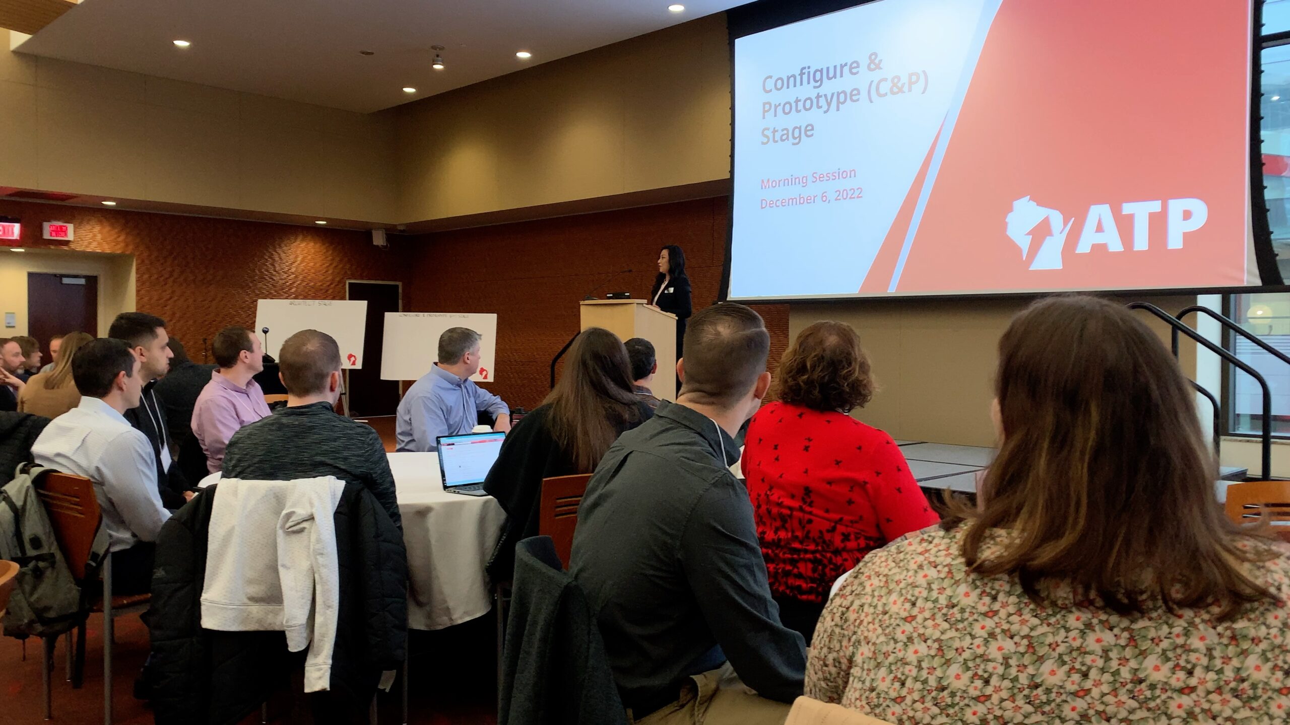 Photo of Dr. Joanna Wang speaking in front of a group of people, with a large Powerpoint on display in the background