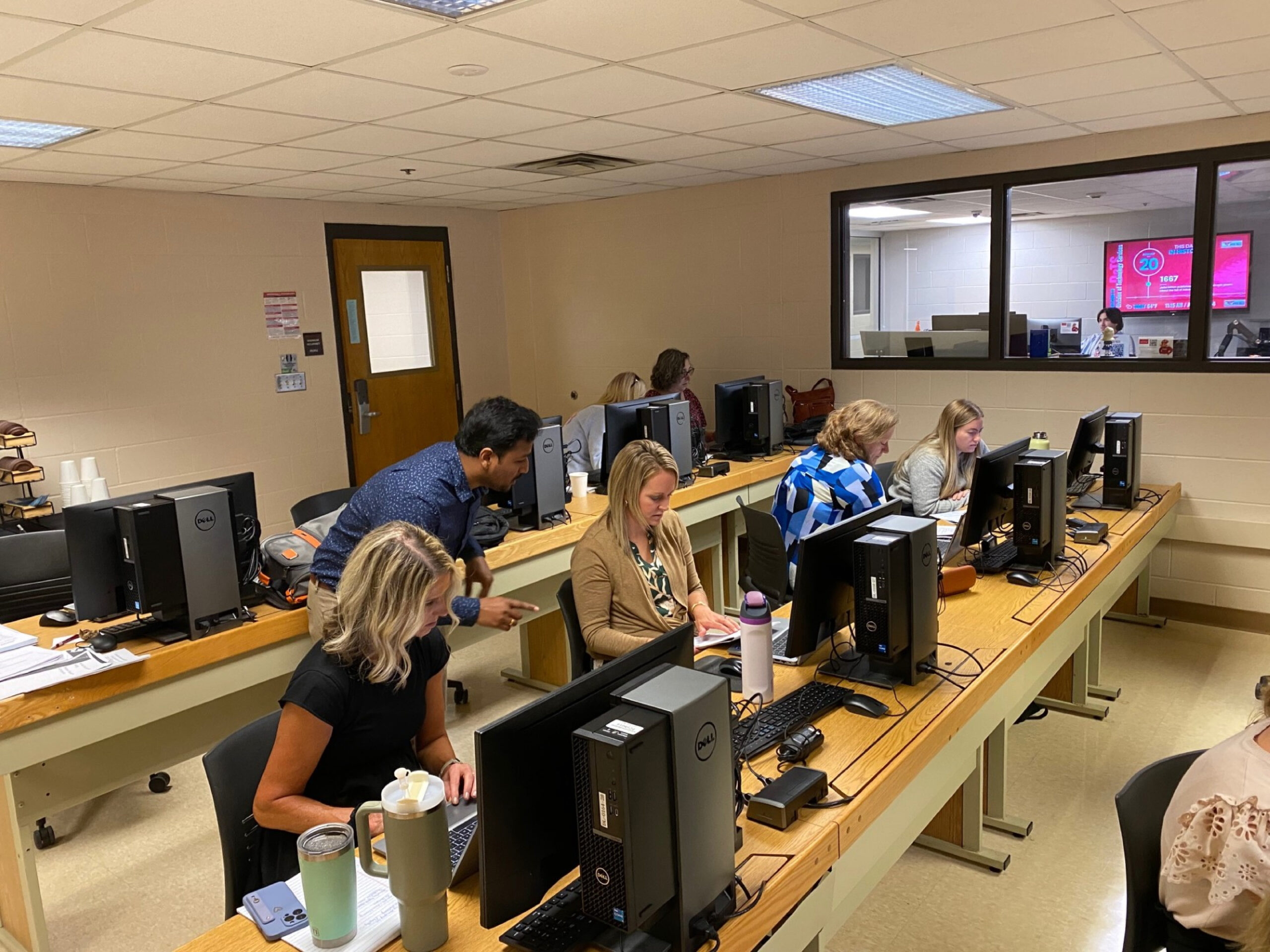 UW-River Falls staff sit in rows and type at computers while a facilitator helps a participant.