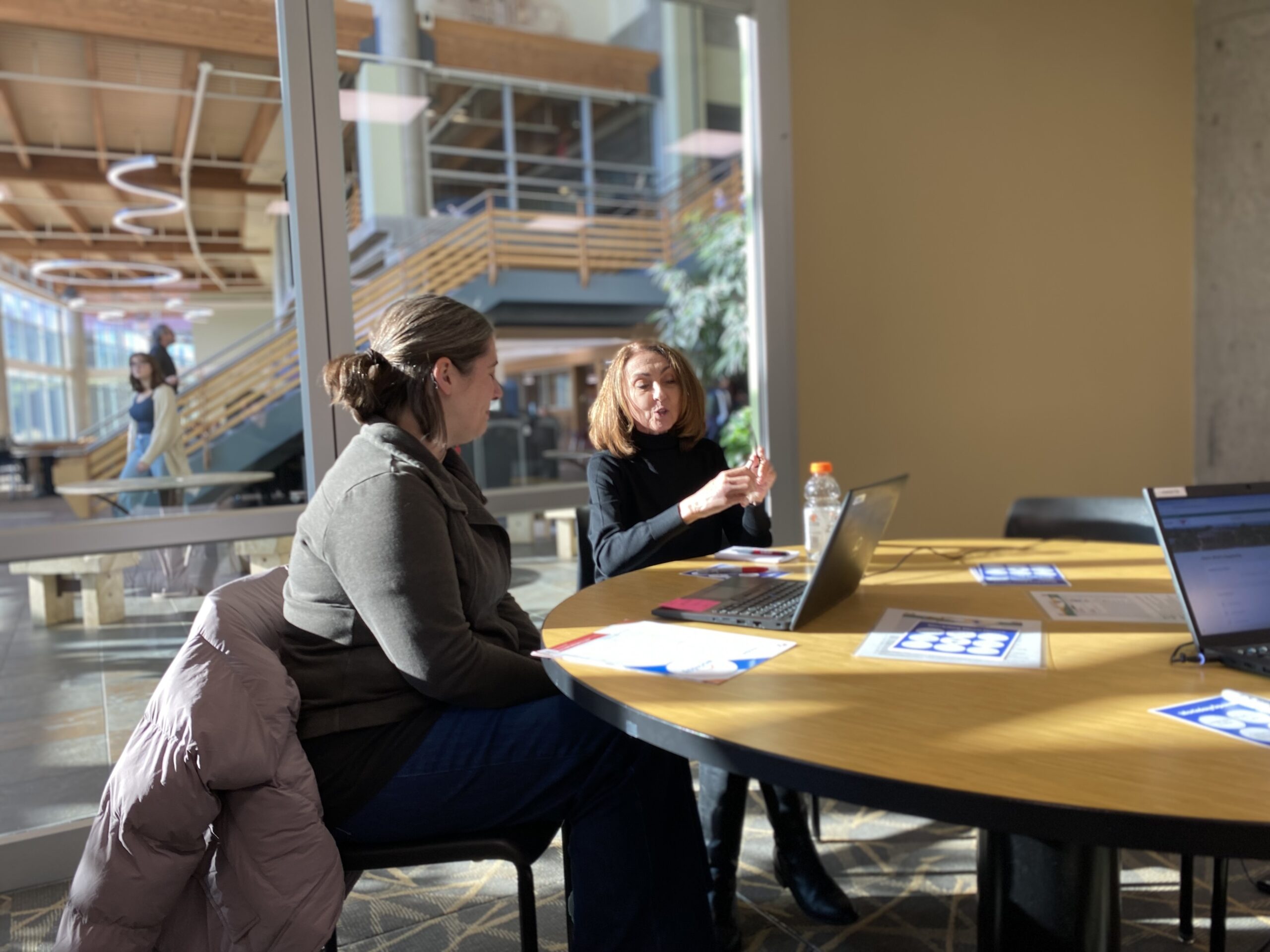 Two UW-River Falls staff talk in front of a laptop in a large room.