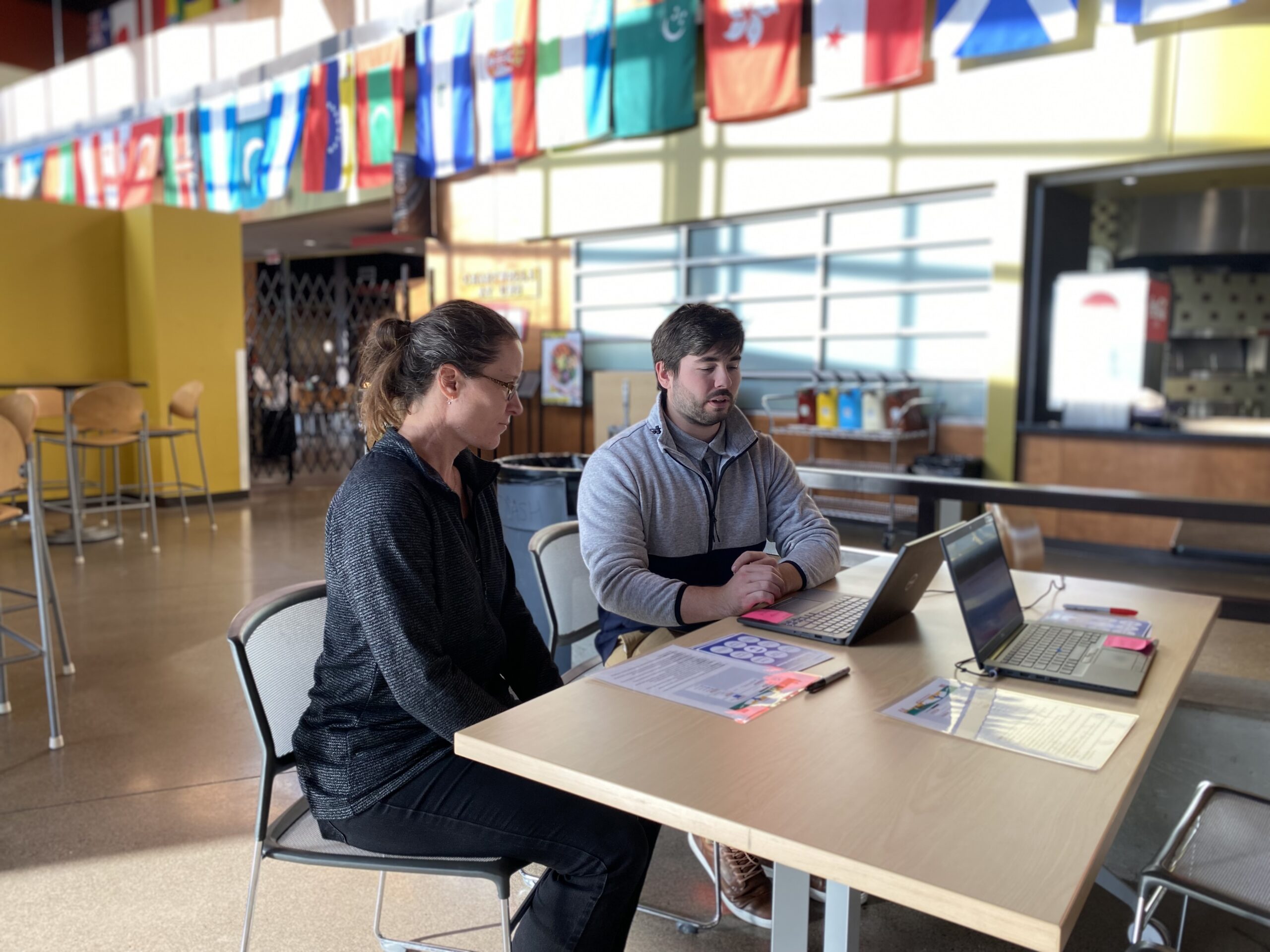 Two UW-Superior staff talk in front of a laptop in a large sunlit room.